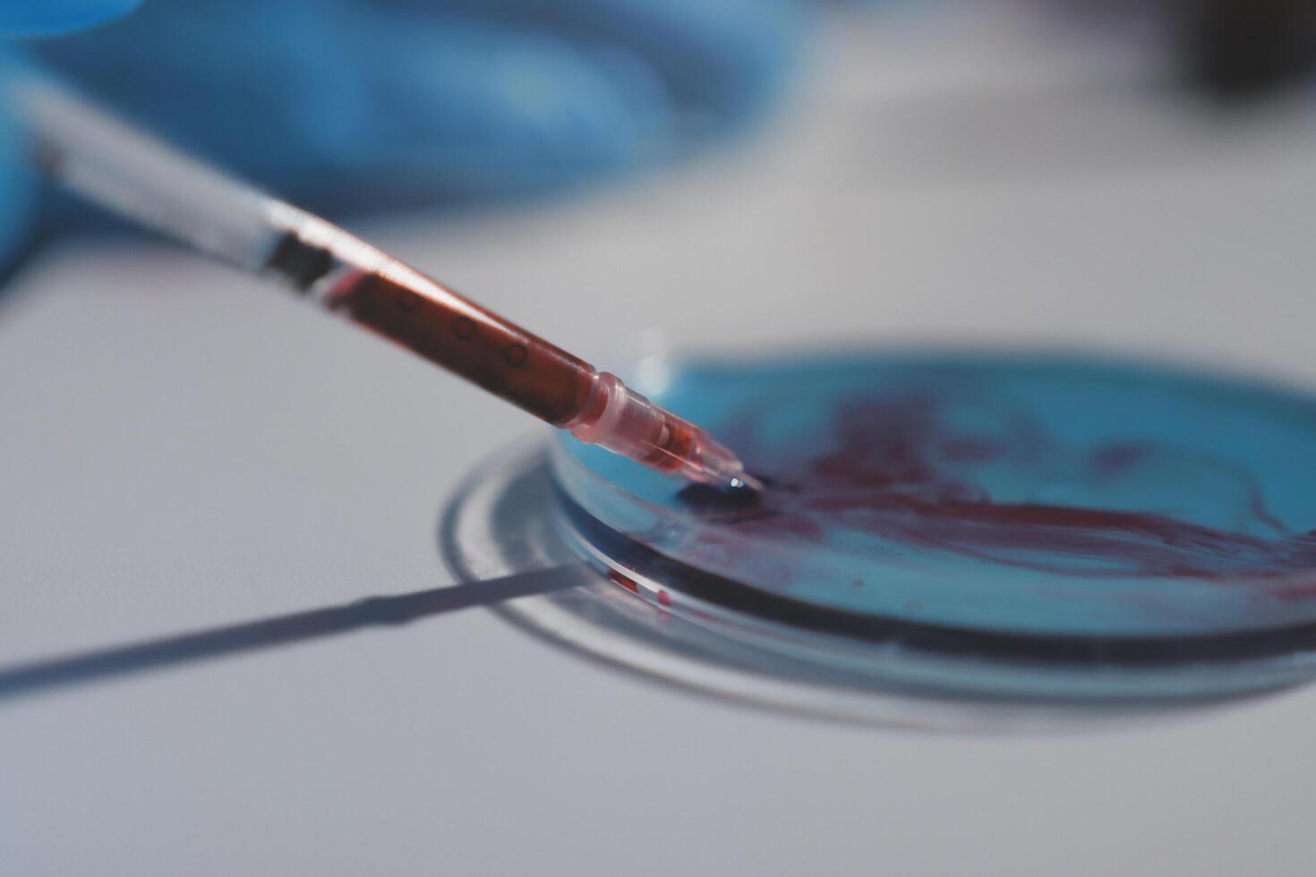 A person in blue gloves holding a pen over a petri dish photo