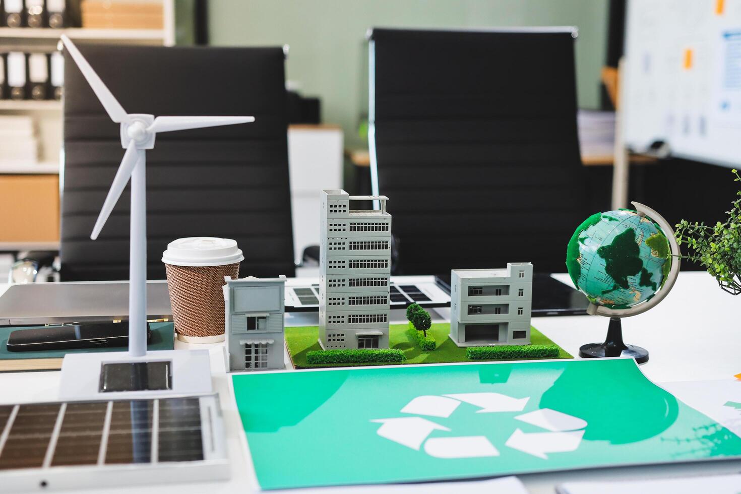 A green recycling sign is placed on a desk with a laptop, a green plant and a wind photo