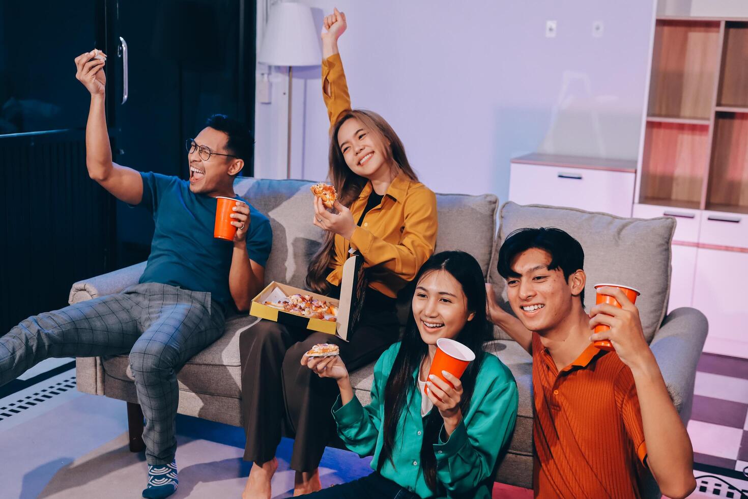 Four friends sitting on a couch with pizza and soda photo