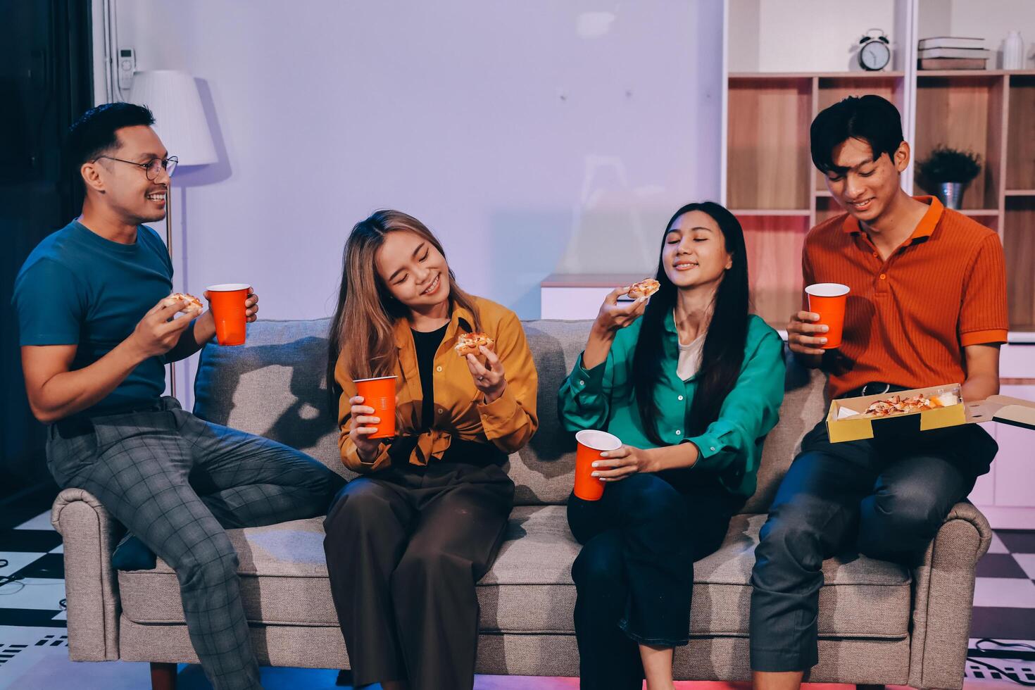 Four friends sitting on a couch eating pizza and drinking soda photo