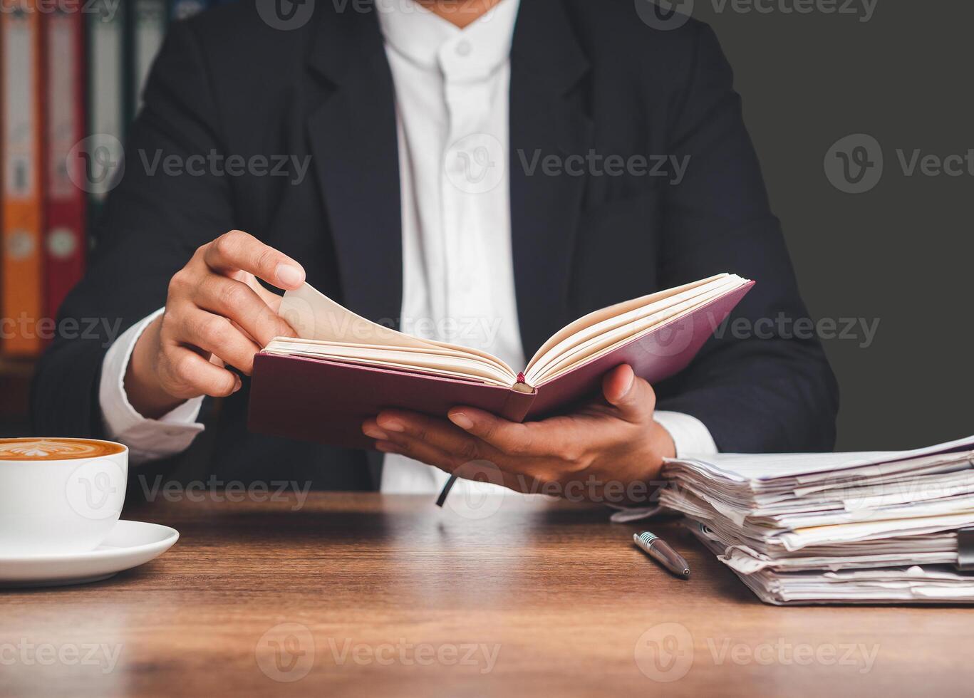 Businessman in a suit holding and reading a book while sitting at the desk photo