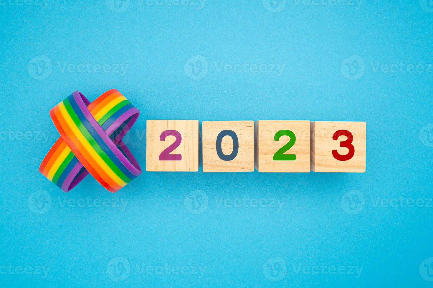 Two rainbow wristbands and wooden cubes with the letters 2023 are on a blue background photo