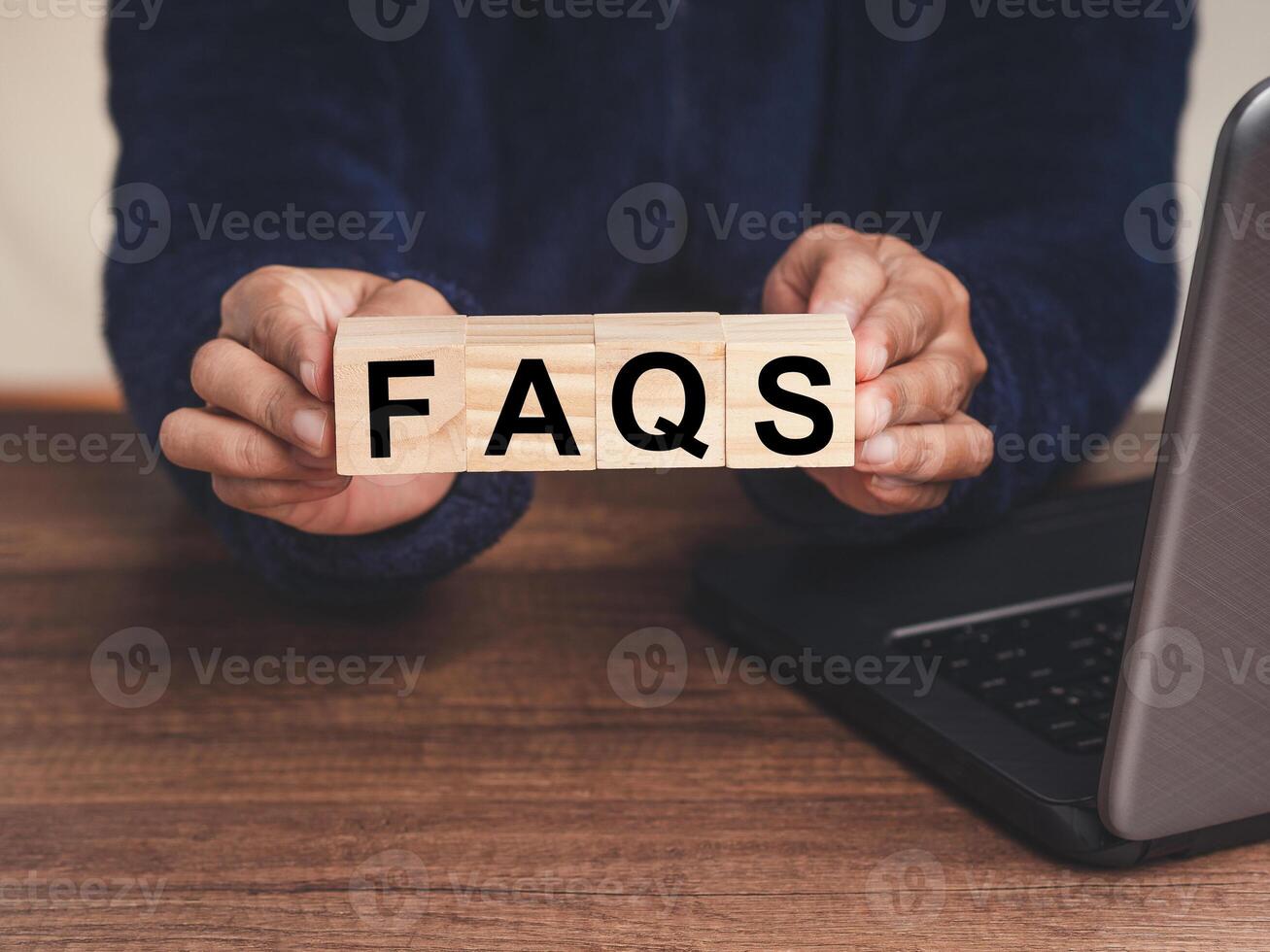 Close-up of hands holding wooden cubes with the letter FAQS while sitting at the table photo