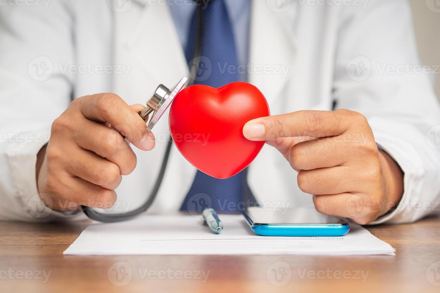 A doctor's hand holding a stethoscope checking a red heart shape symbol mockup while sitting in the hospital or clinic photo