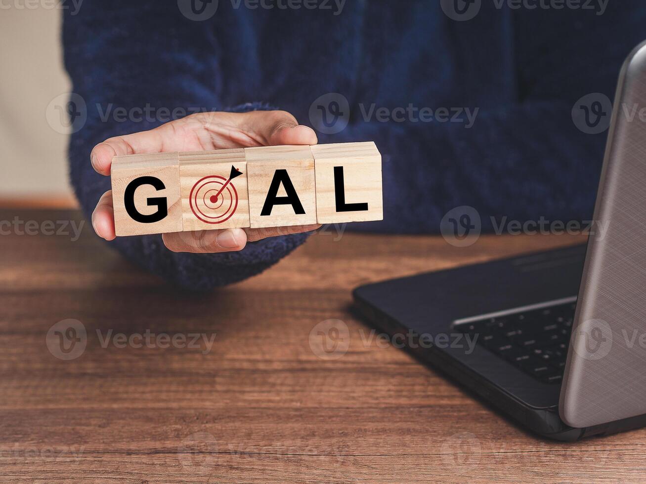 Close-up of hand holding wooden cubes with letters GOAL and dartboard icon while sitting at the table photo