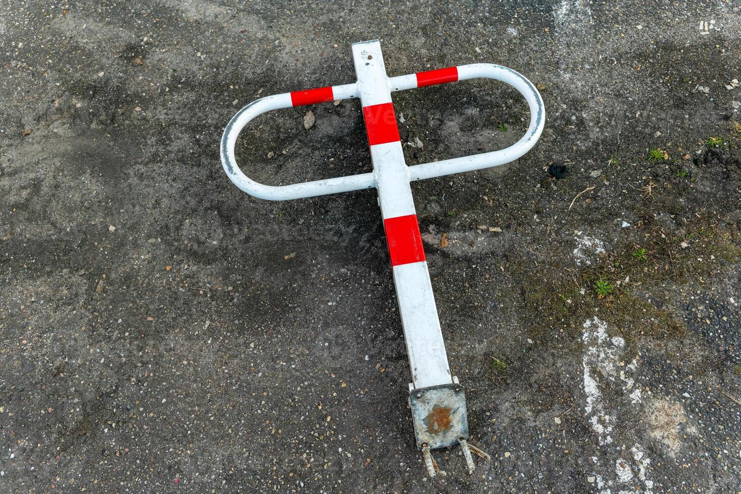 Broken parking barrier laying on the ground with red and white stripes in an urban area on a cloudy day photo