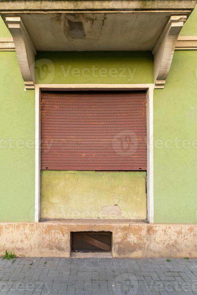 Abandoned storefront with a closed shutter in a vibrant green facade in a quiet urban setting photo