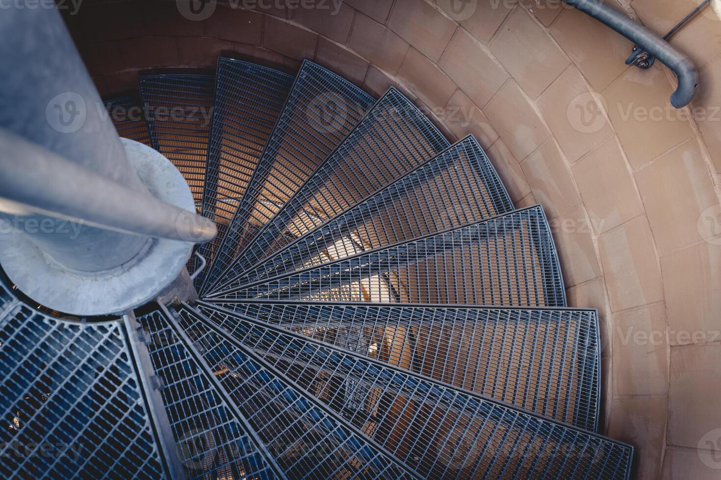 Spiral staircase with metal steps and a circular design captured from a high angle at sunset photo