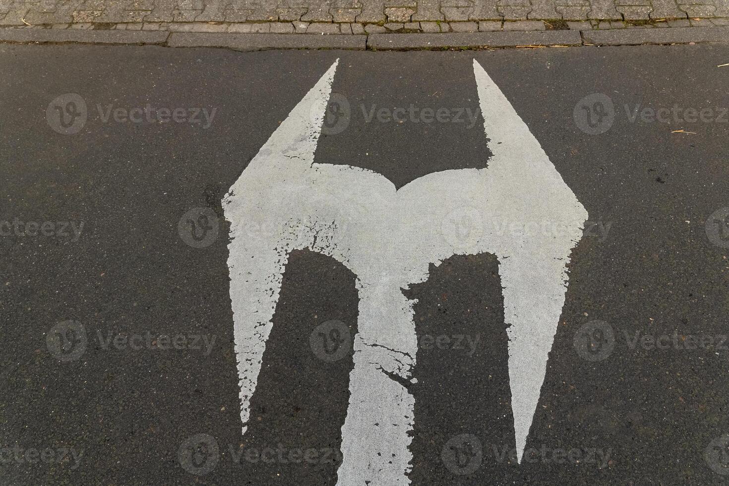 White marking resembling a logo on asphalt near a brick sidewalk in an urban setting photo