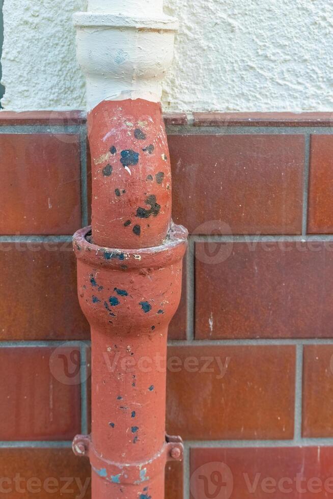 Rusty water pipe with chipped paint against tiled wall in urban setting under evening light photo