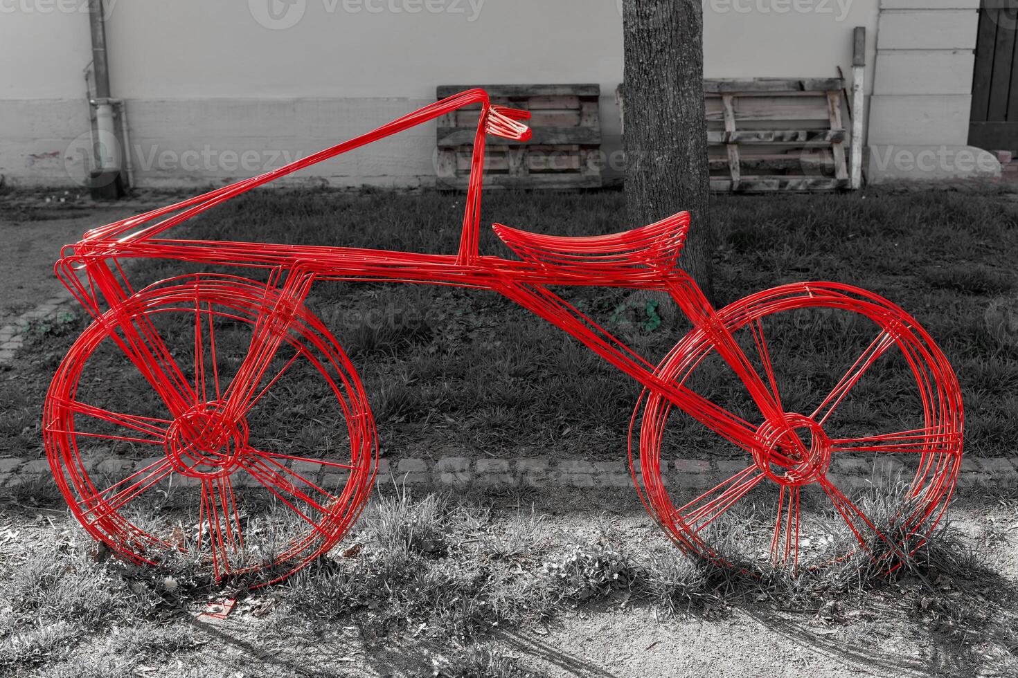 Creative red wire bicycle sculpture displayed on the sidewalk next to a grassy area in an urban setting photo