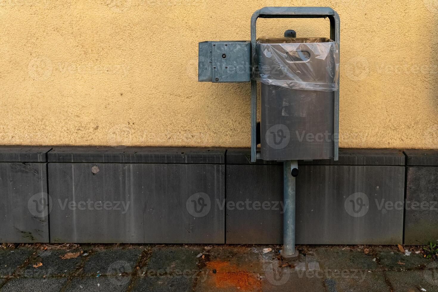Metal waste container attached to a wall in an urban setting during daylight hours photo