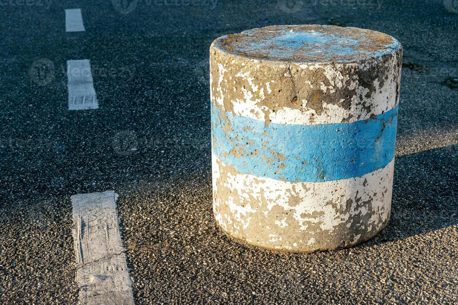 Concrete barrier with blue stripe on a sunlit asphalt road in a quiet urban setting during late afternoon photo