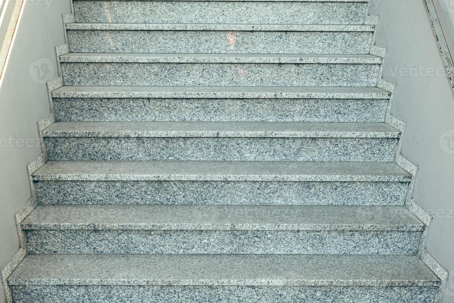 Steps made of polished granite leading up to a well-lit interior in a modern building during daylight hours in an urban setting photo