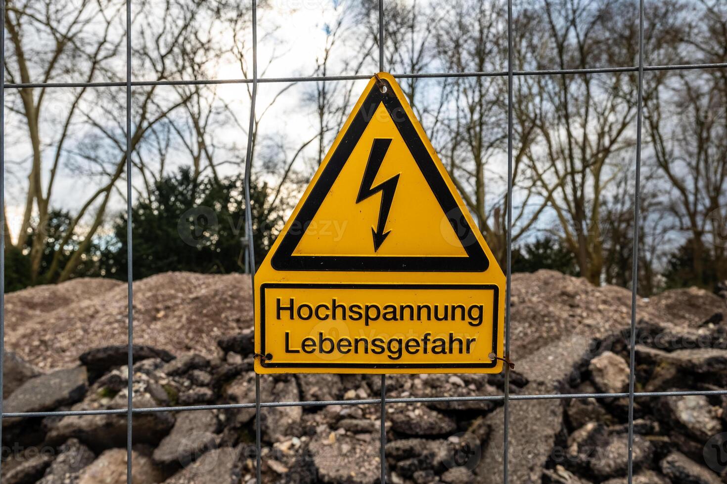 Caution sign warning of high voltage danger with the german words high voltage life threatening near a construction site during cloudy weather photo