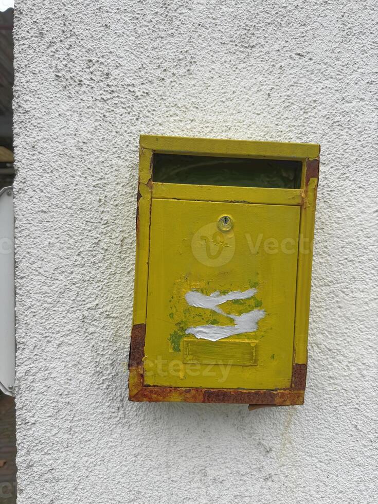 Weathered Yellow Mailbox on White Wall photo