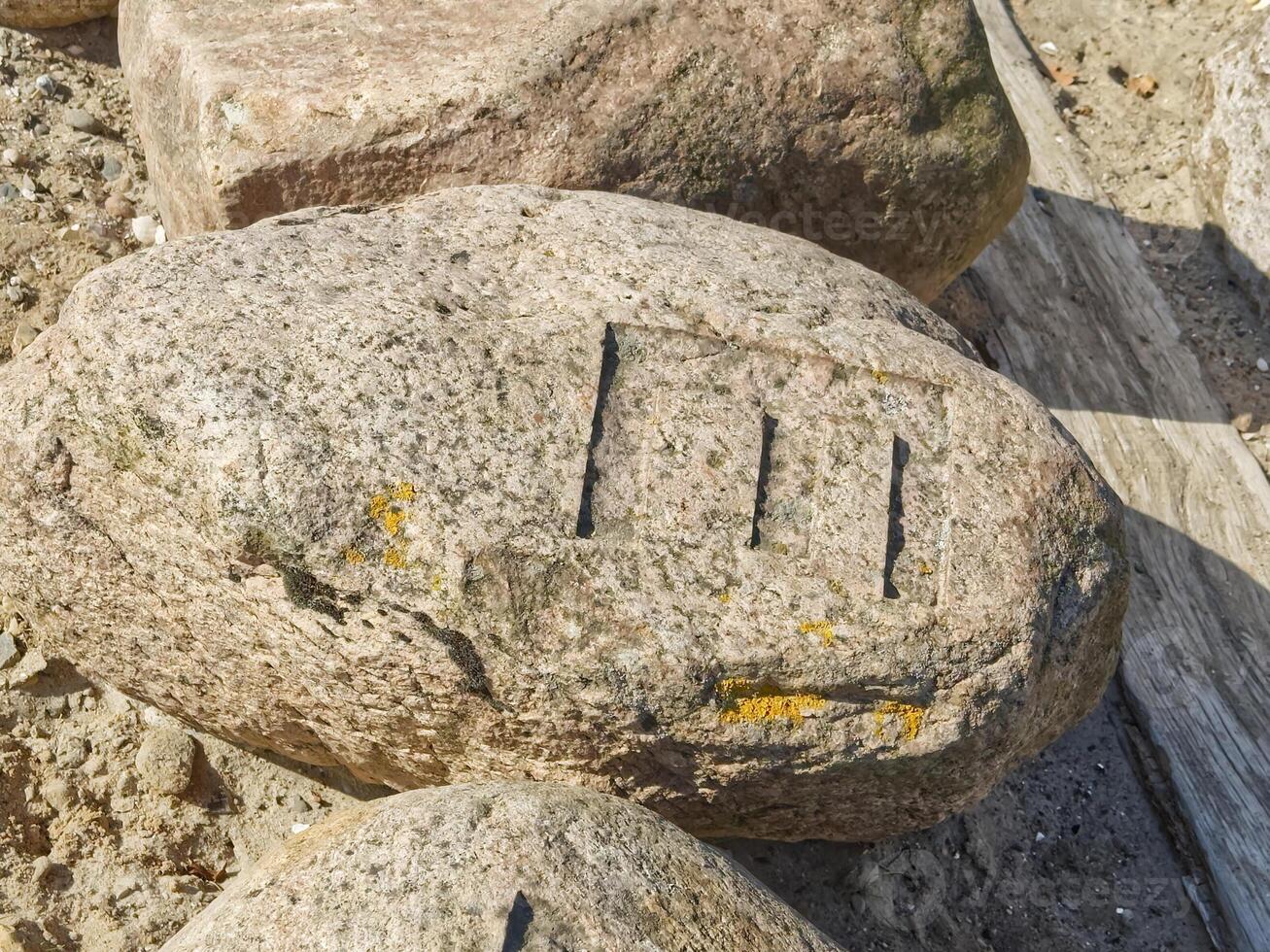 A closeup view of a large, weathered rock with distinct markings on its surface. The rock is surrounded by other stones and has some yellow lichen growth. The markings appear to be carved lines photo