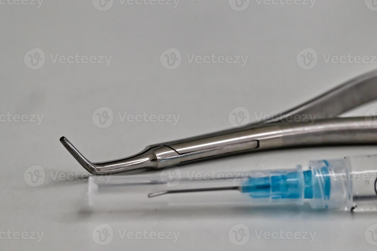 A close-up of dental tools including a curved dental instrument and a syringe with a needle, placed on a light surface. photo