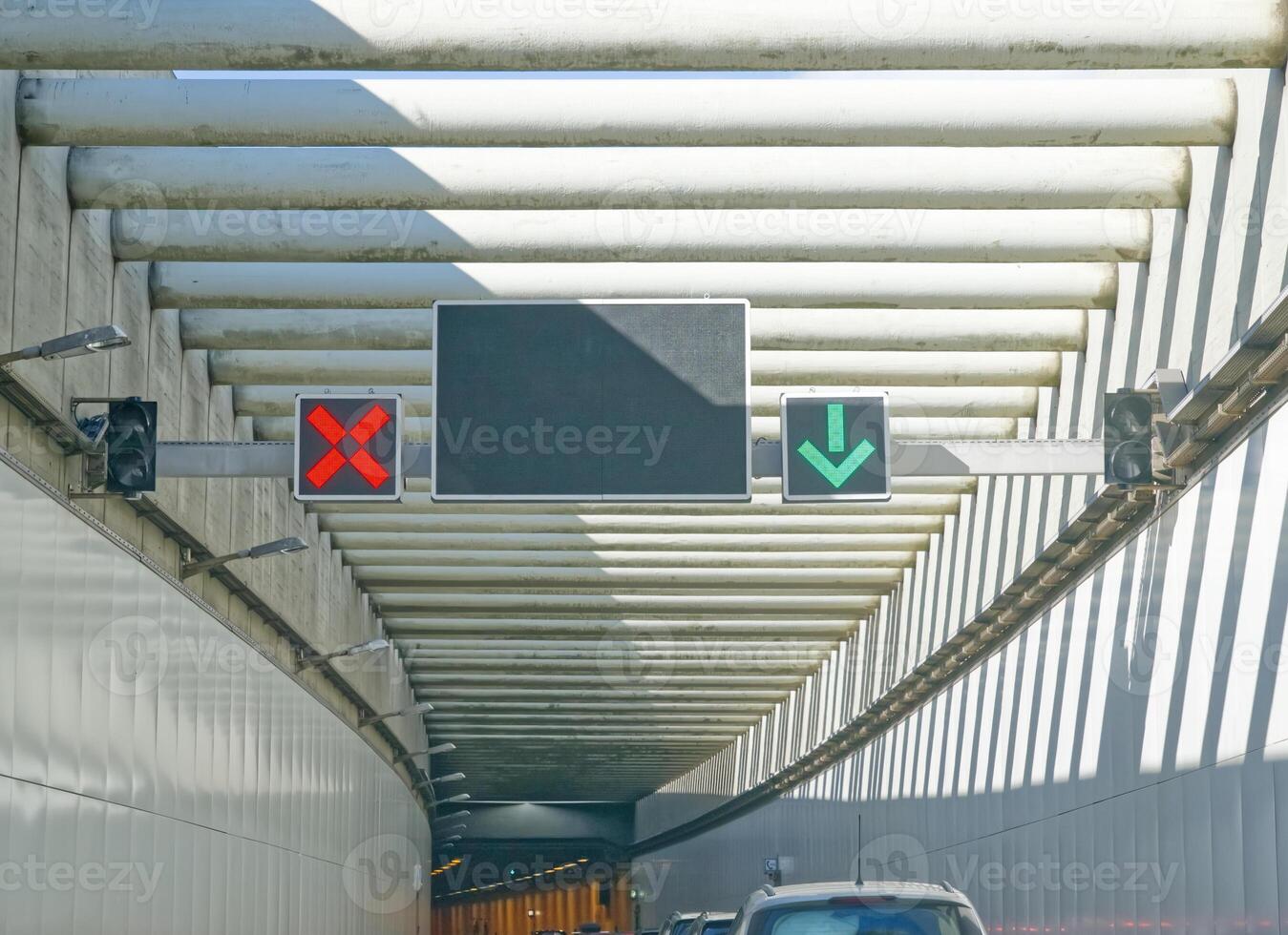 Traffic lights indicating lane usage in a tunnel, with a red X signal and a green downward arrow. The tunnel has a modern design with overhead beams and a clear road ahead. photo