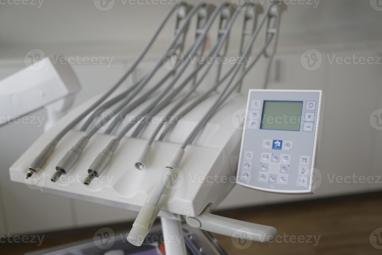 A close-up view of a dental chair control panel with multiple hoses and a digital display, set in a modern dental clinic environment. photo