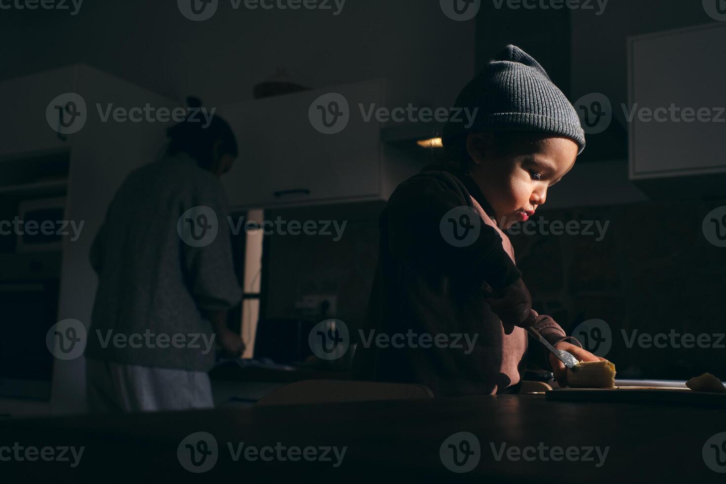 Focused little boy cutting banana on board near anonymous mother photo