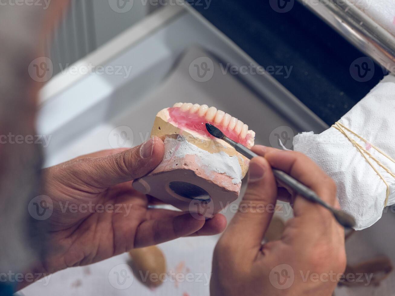 Crop dentist technician applying steel spatula on jaw implants photo