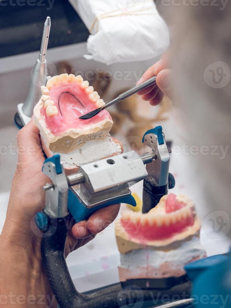 Crop senior dental technician shaping denture with spatula photo