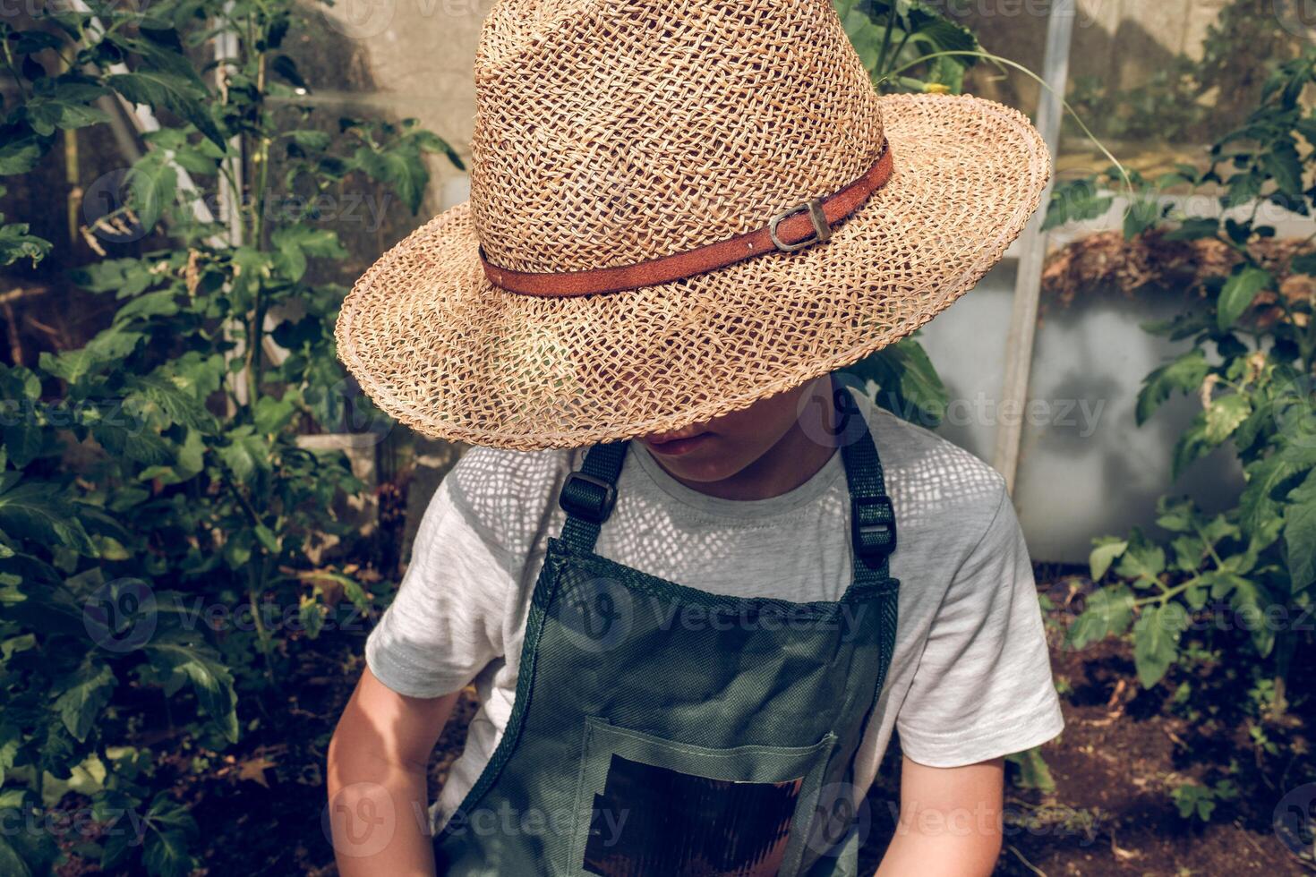 Preteen boy sitting in garden bed in straw hat photo
