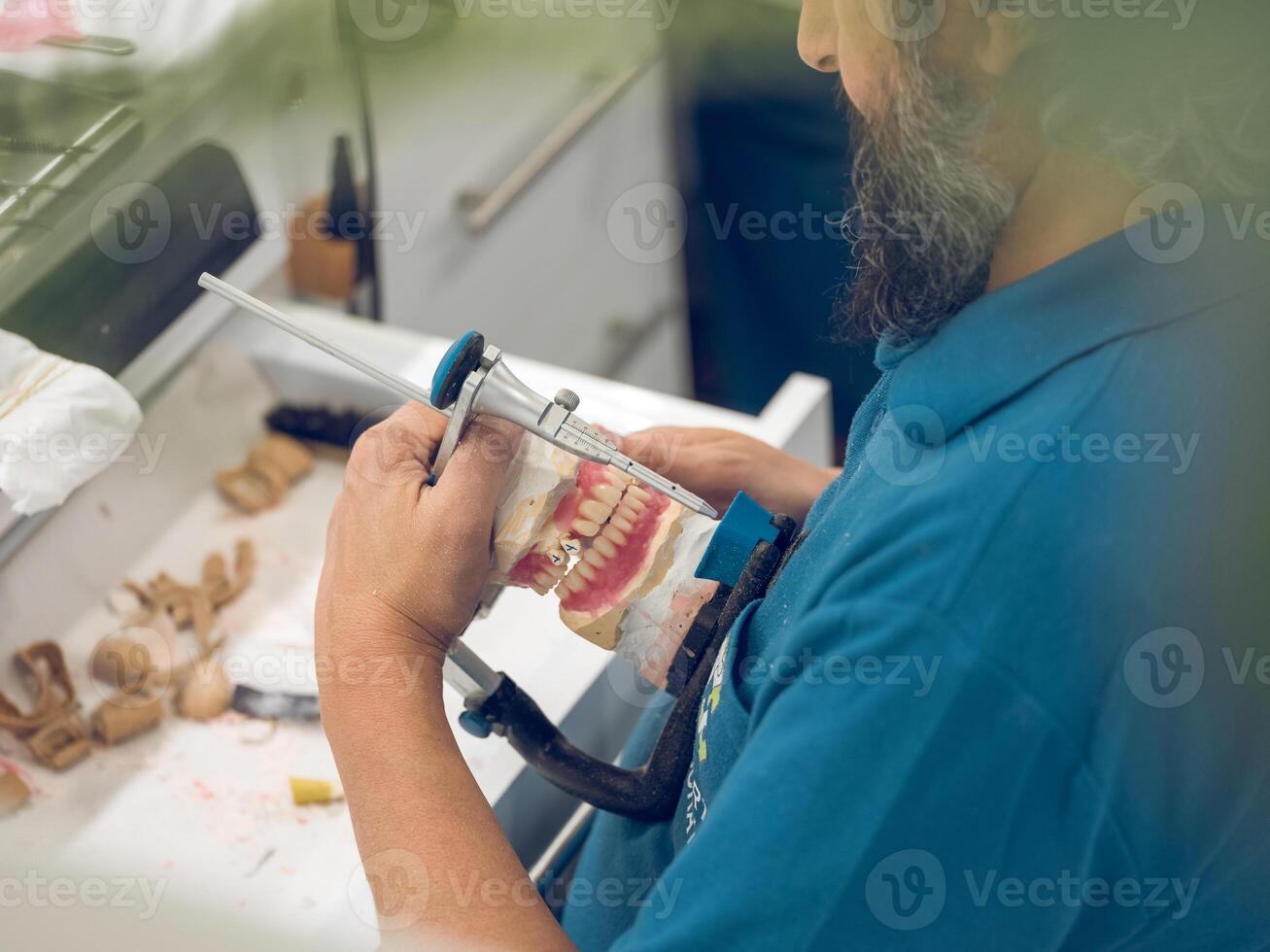 Crop senior male technician fixing jaw dentures in articulator photo