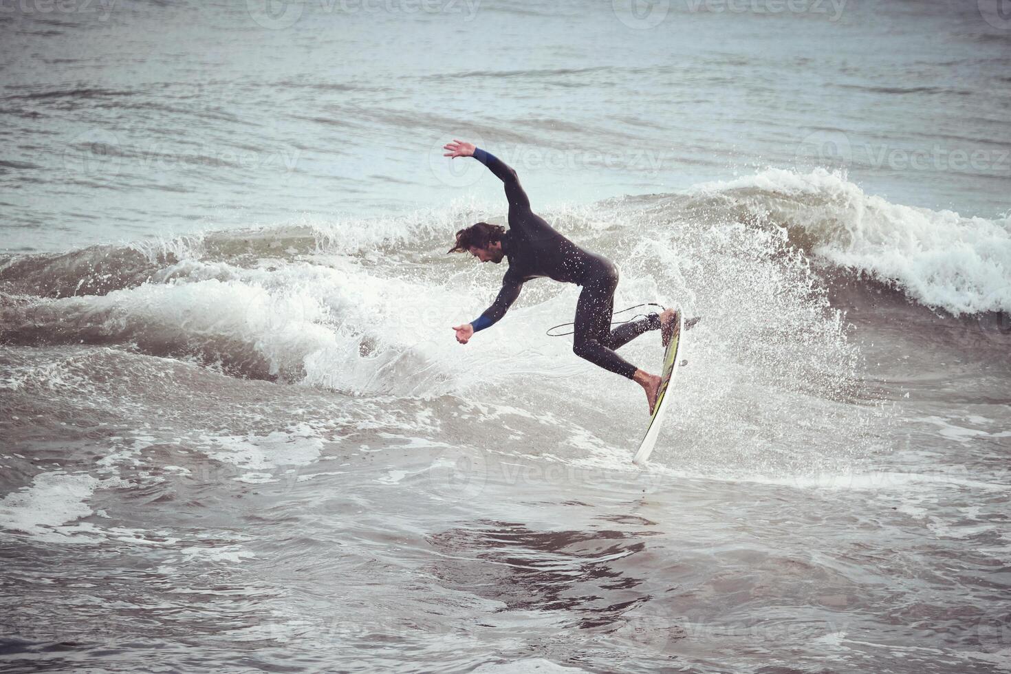 Surfer male jumping on wave standing on surfboard in ocean photo