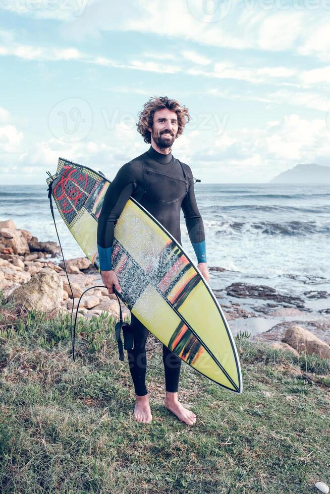 Smiling Hispanic sportsman standing at seaside with surfboard photo