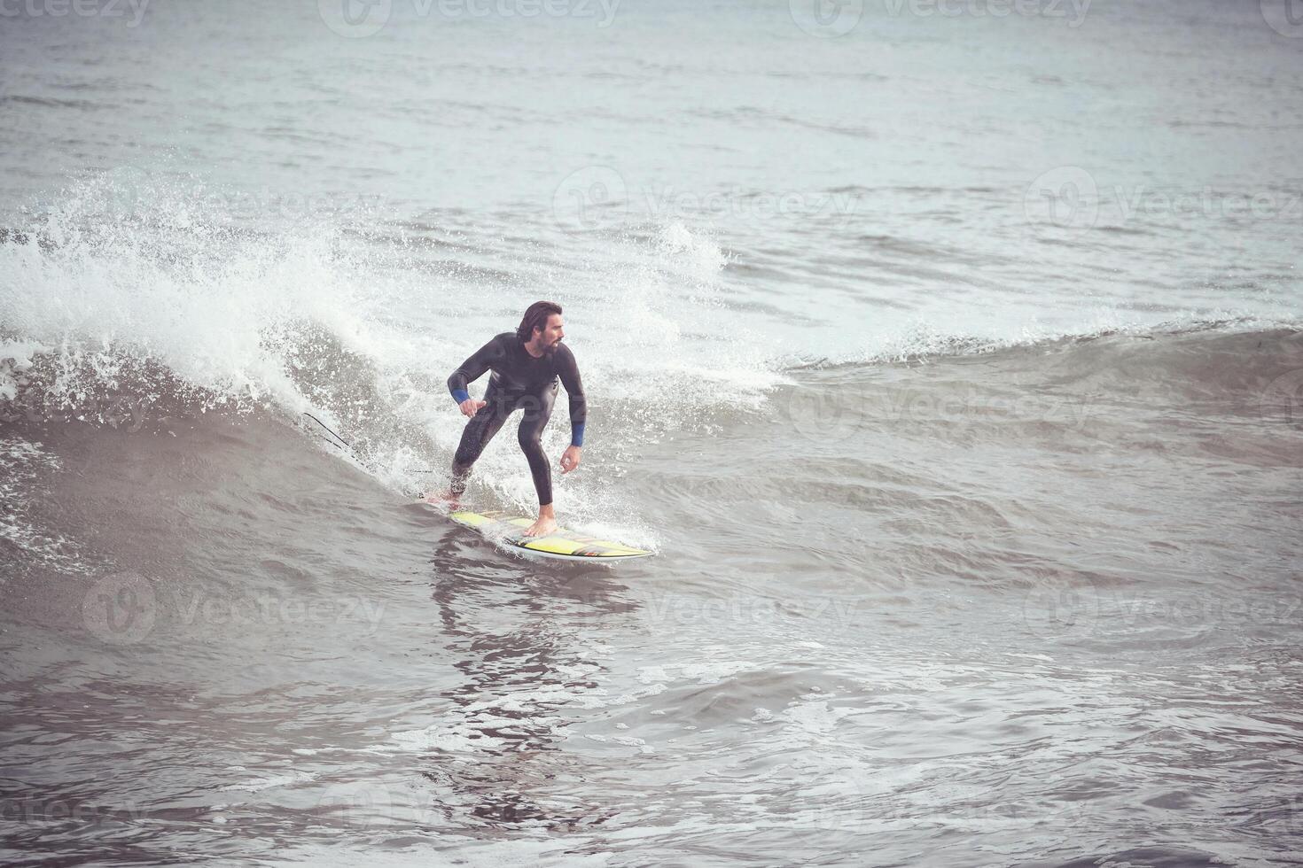 Surfer in wetsuit riding on wave on surfboard in ocean photo