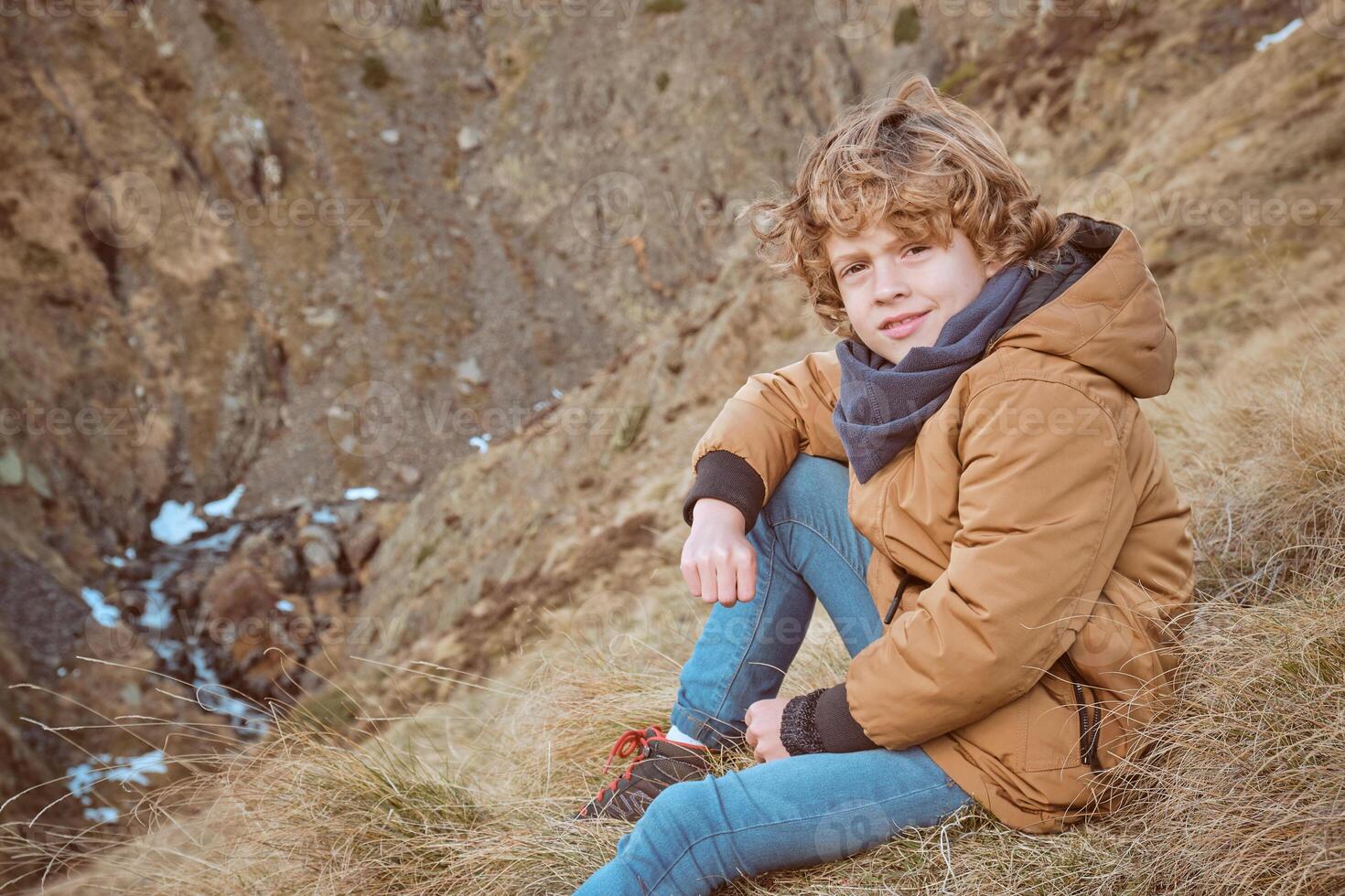 Smiling boy in warm clothes sitting on grassy hill photo