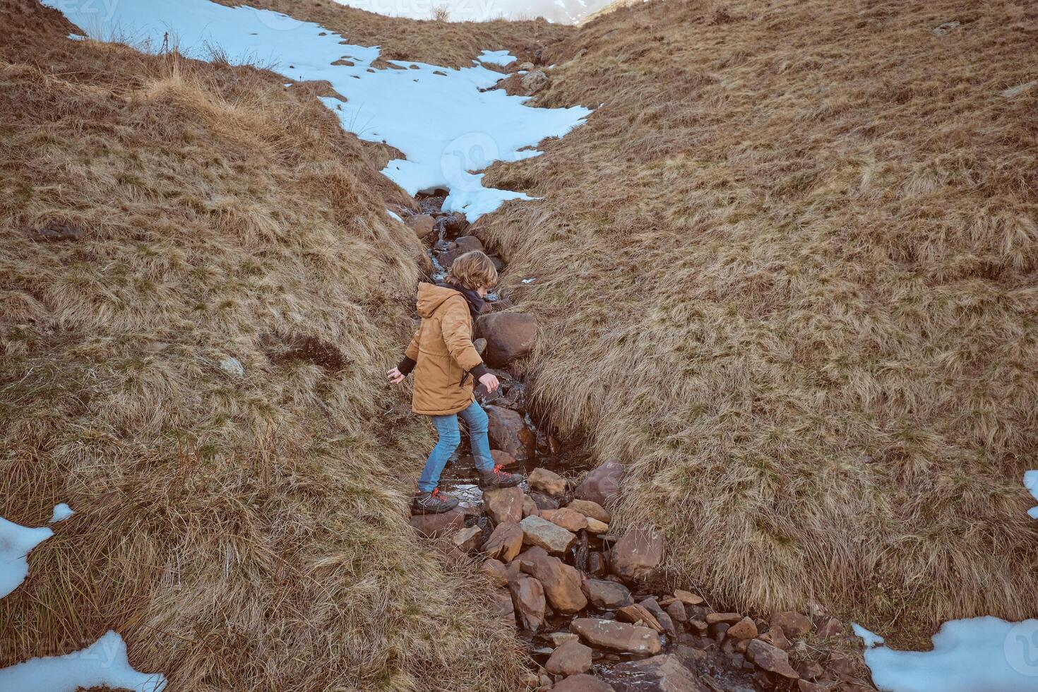 Unrecognizable boy stepping over creek on field with snow photo