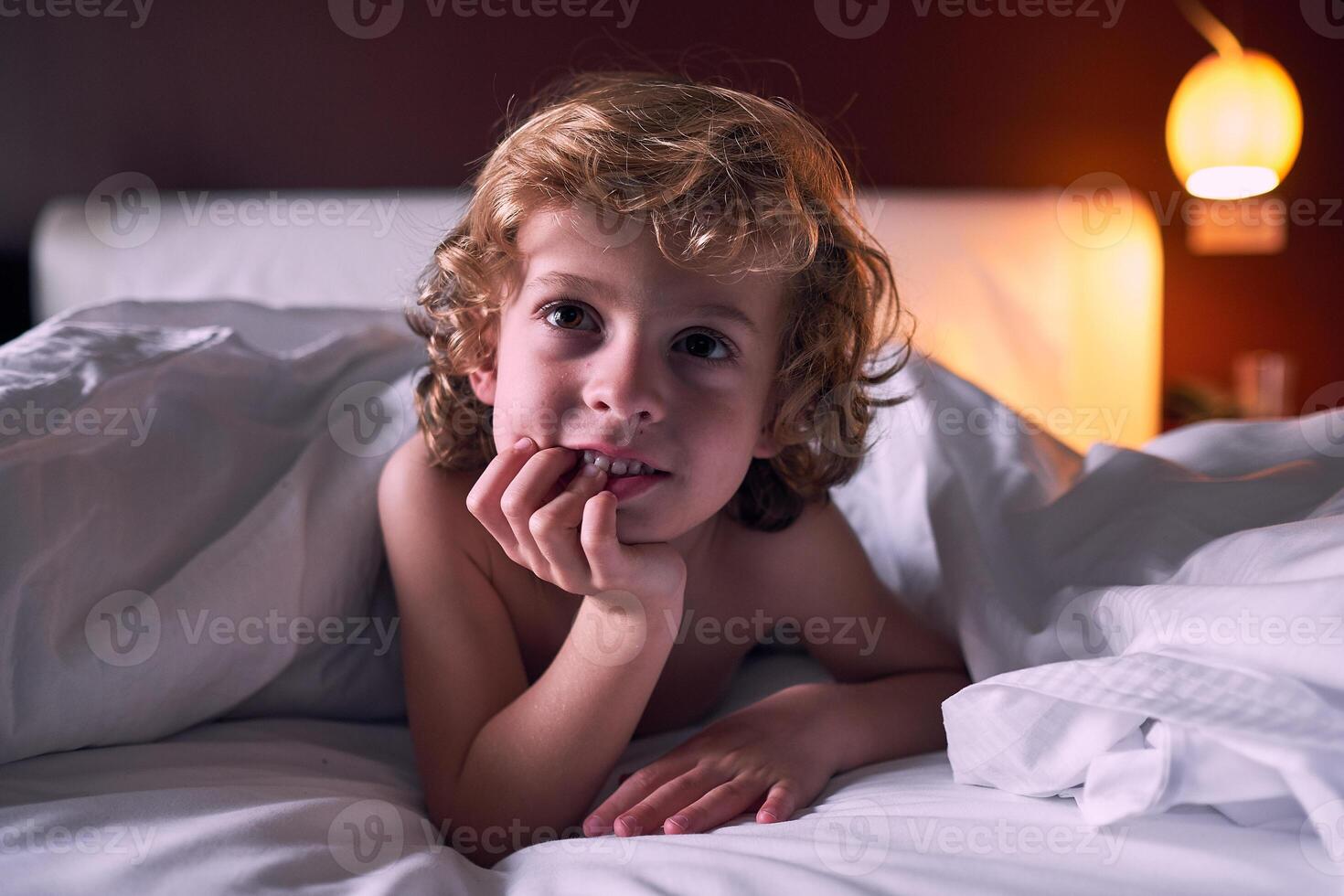 Curious little boy lying on bed under duvet photo