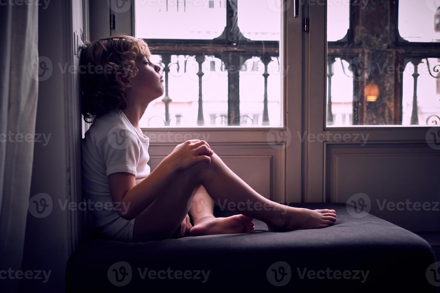 Peaceful kid napping on pouf near window photo