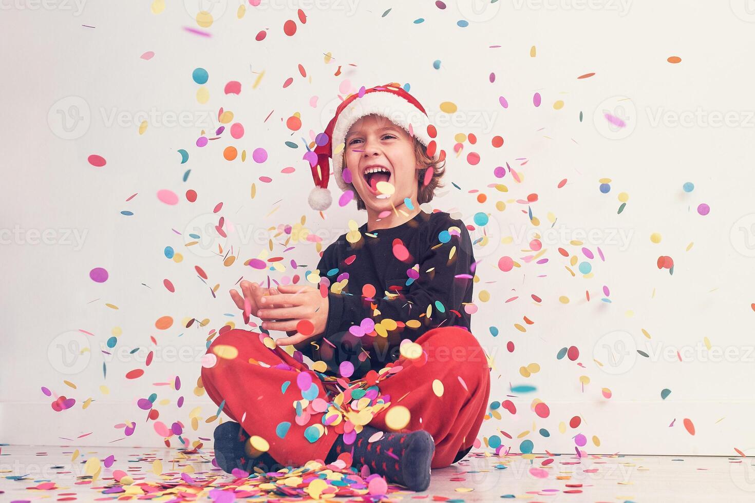 Smiling boy in Santa hat under colorful confetti photo