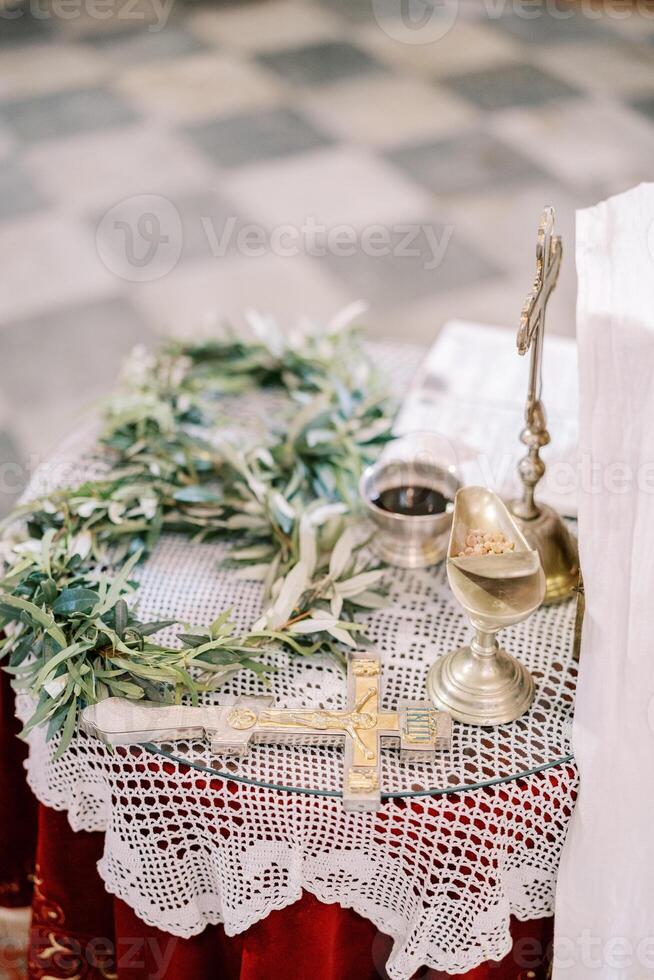 Wreaths lie next to a crucifix, a cup of wine on a table in a church photo