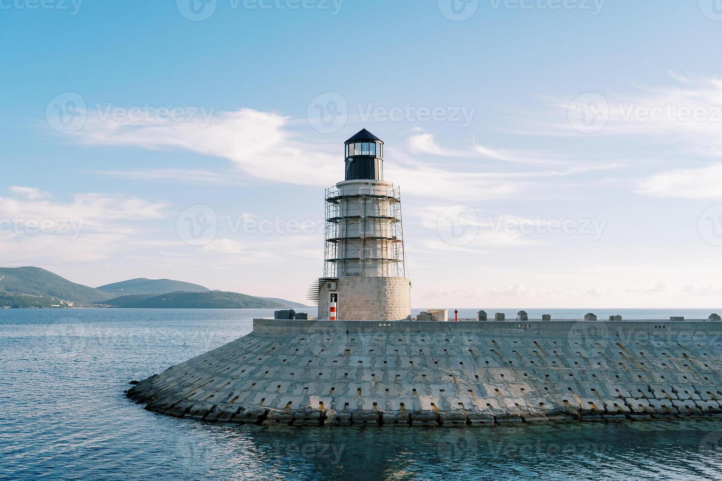 Lighthouse on a breakwater in the sea against the backdrop of a mountain range photo