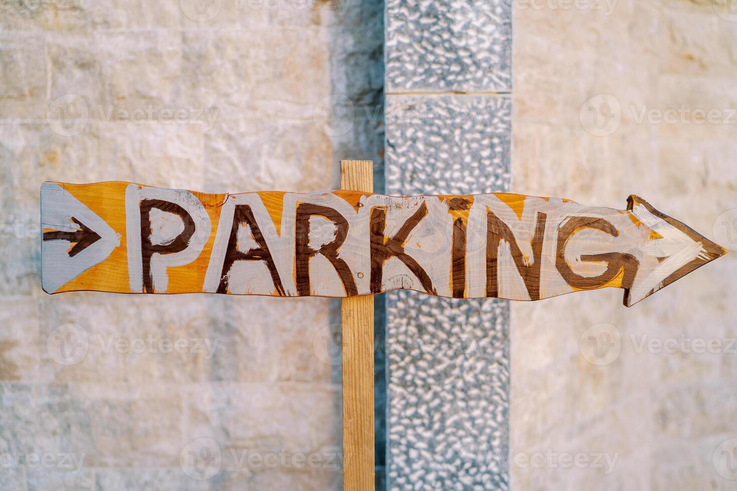 Wooden pointer with an arrow near the stone wall. Caption. Parking photo
