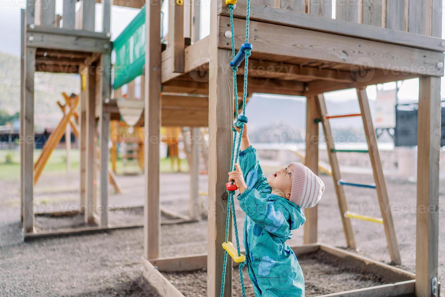 Little girl reaching up to the top rung of the rope ladder in the playground photo
