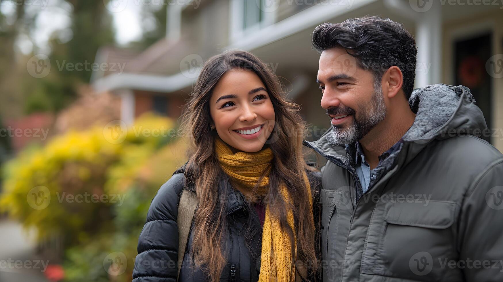 Happy young Latin couple with a realtor walking in a suburban neighborhood, pointing at houses, photo