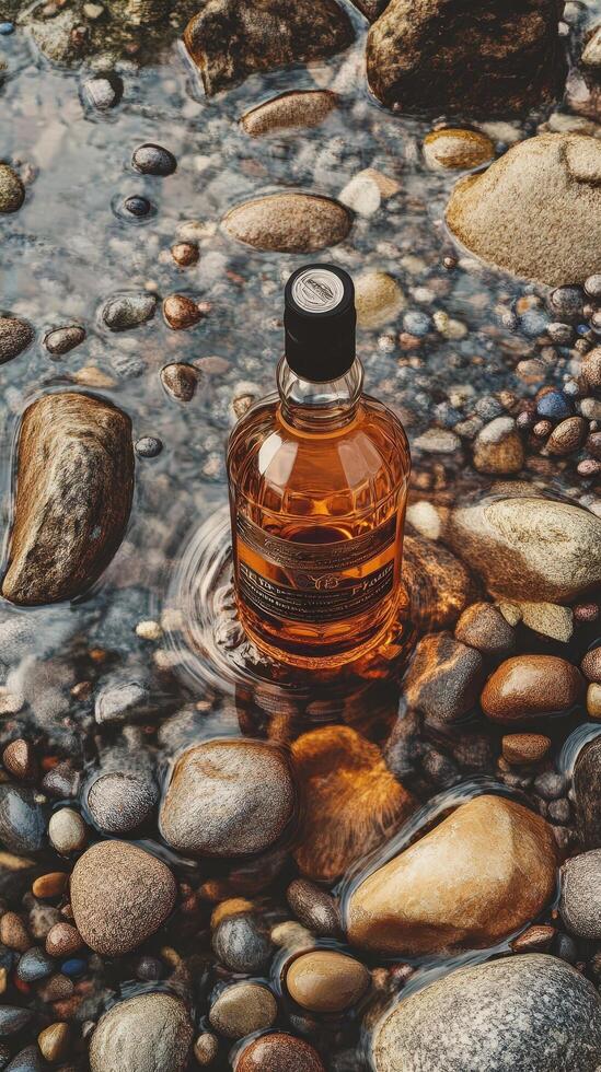 A bottle of whiskey sitting on the rocks in a stream photo