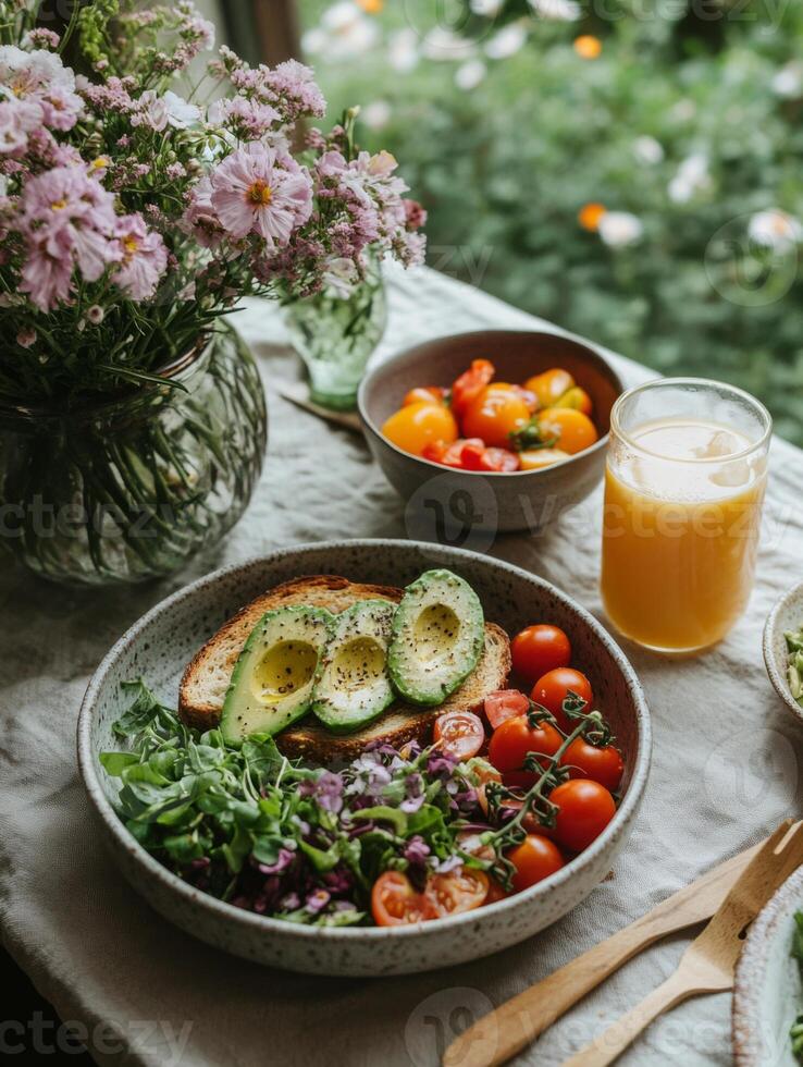 Fresh salad with tomatoes, avocado, and bread on table with flowers and juice. vibrant and healthy meal surrounded by nature beauty photo