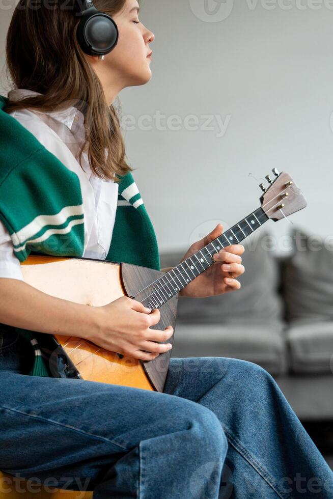 Woman enjoy music, playing balalaika, listening to songs through headphones at home. Ear training photo