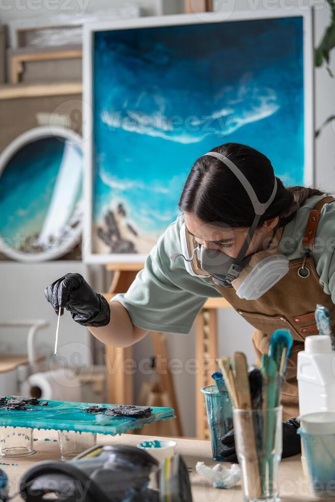 Attentive thorough woman working carefully with epoxy resin, creating making artwork painting. photo