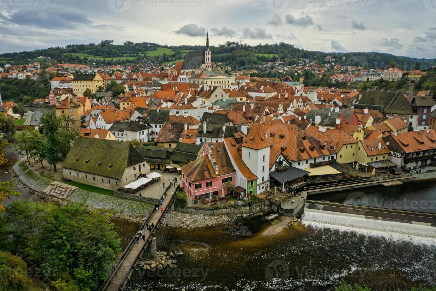 An aerial view of Krumlov in autumn reveals a vibrant tapestry of fall colors, with the historic town nestled along the winding Vltava River. photo