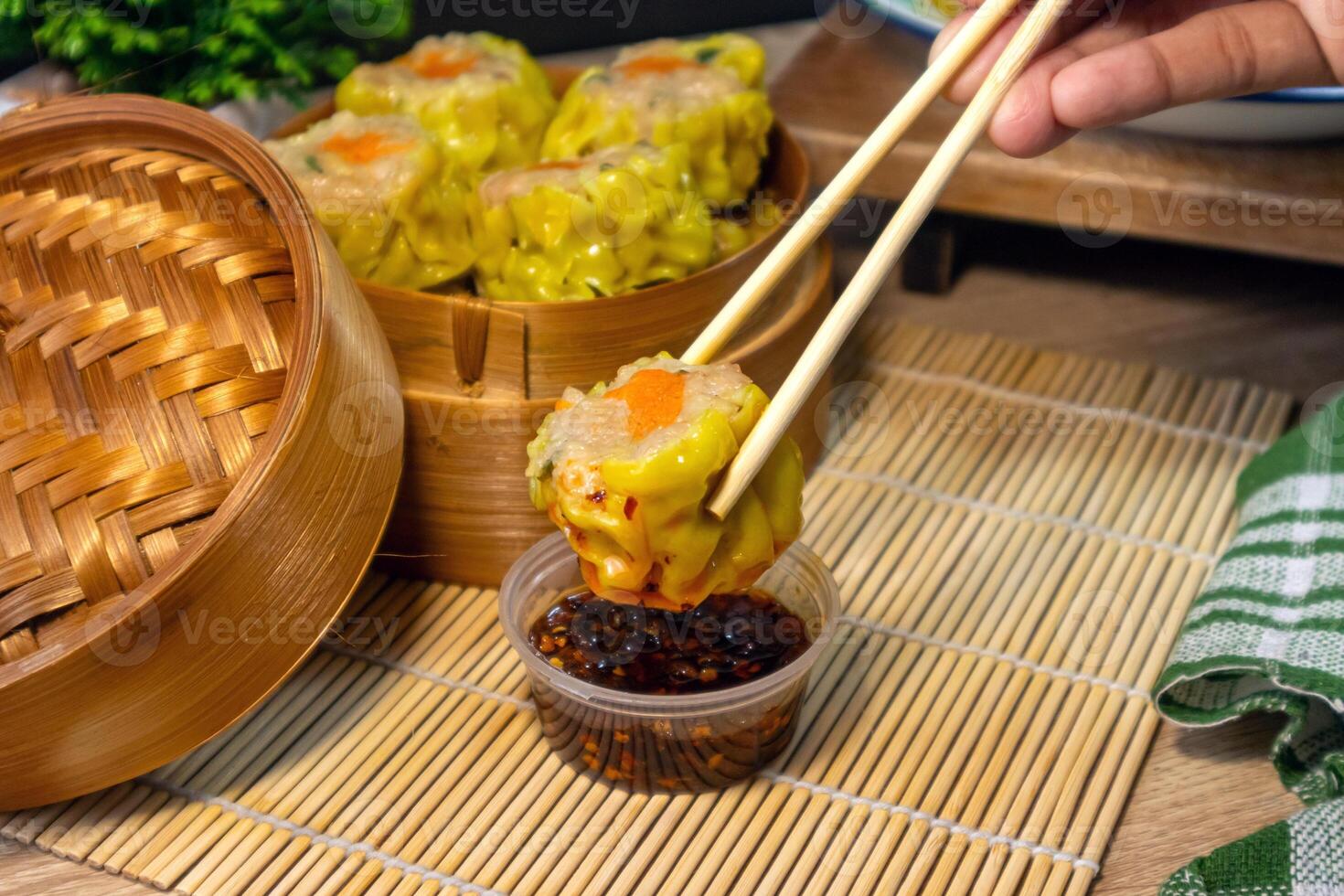 Hand holding dim sum with chopsticks and dipping it in chili oil. A traditional Chinese food. photo