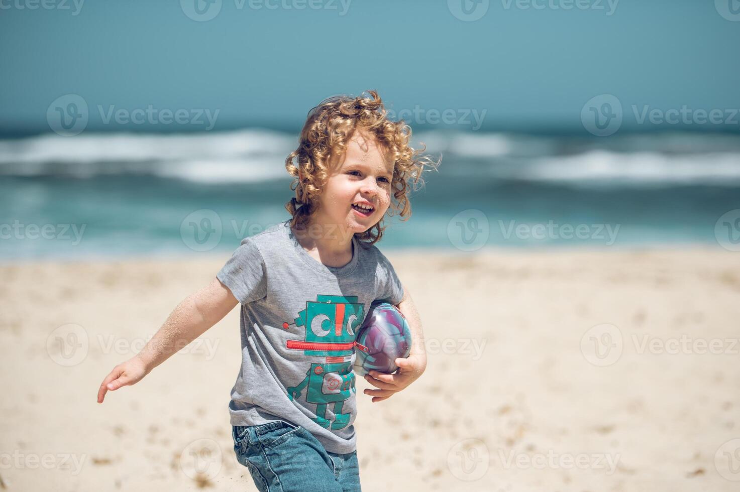 Cheerful boy with ball walking on beach photo