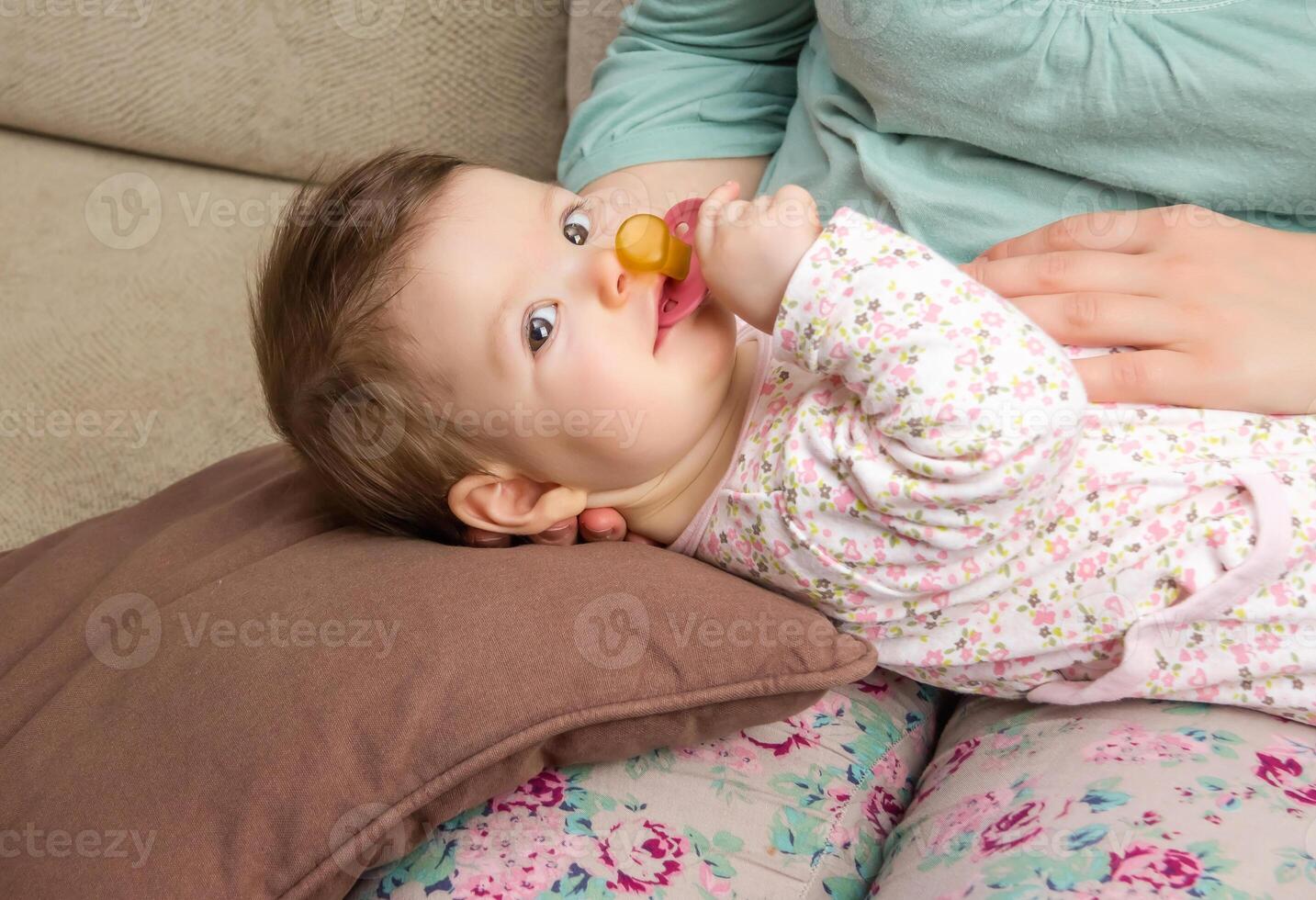 Baby playing with pacifier lying over mother legs photo